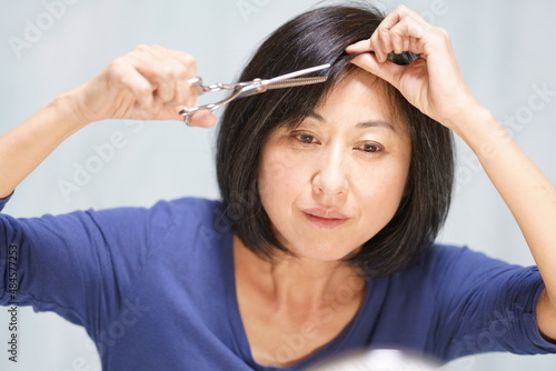 セルフカットするミドル女性　ハサミを持って自分の前髪を切る中年女性　上半身 photo