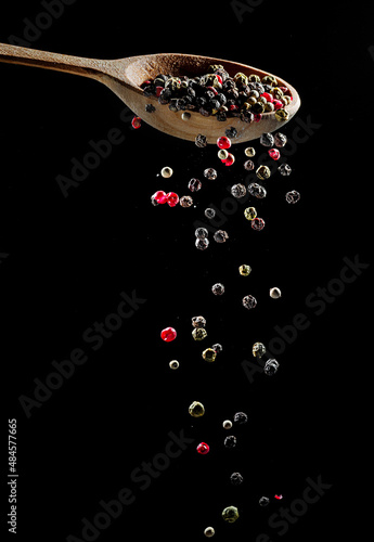 Fotografie Mix of peppercorns falling down from the wooden spoon at black background