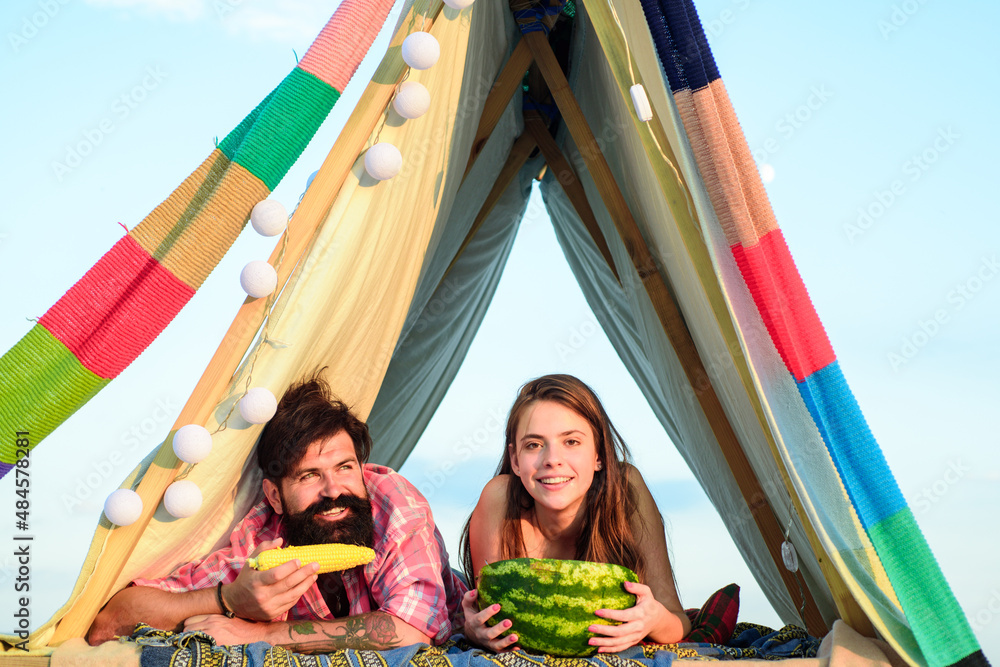 Fototapeta premium Romantic couple eat watermelon in tent on camping. Outdoor adventure with friends on nature. Organic food.