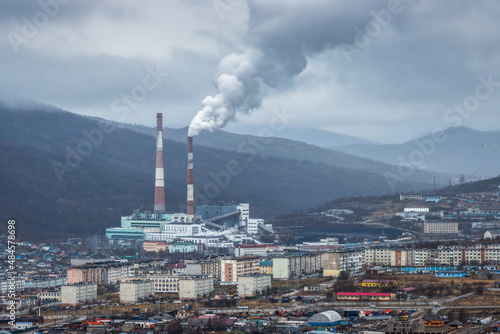 Urban industrial landscape. Top view of residential buildings and thermal power plant. Thick puffs of smoke from the factory chimney. Cloudy rainy weather. Magadan, Magadan region, Siberia, Russia.