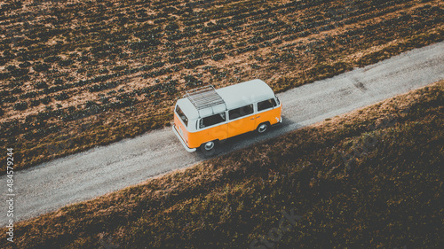Volkswagen Van combi vw t2 - vanlife - une vue aérienne d'une camionnette de style vintage orange et blanche circulant sur une route à travers ce qui semble être une zone sèche photo