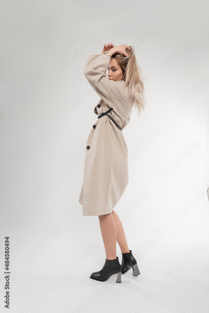 Fashion pretty young elegant woman with beige stylish coat and classic leather shoes poses in studio on a white background Fashion pretty young elegant woman with beige stylish coat and classic leather shoes poses in studio on a white background