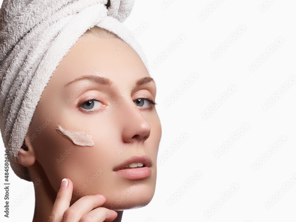 Beautiful face of young woman with cosmetic cream on a cheek. Skin care concept. Closeup portrait isolated on white. Close-up young beautiful face of girl applying moisturize cream Beautiful face of young woman with cosmetic cream on a cheek. Skin care concept. Closeup portrait isolated on white. Close-up young beautiful face of girl applying moisturize cream