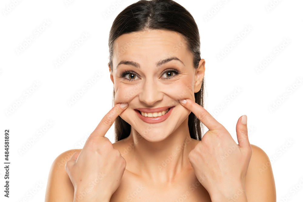 Young woman forcing her smile with her fingers on white