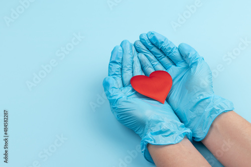 Red heart in hands in blue medical gloves on blue background. Background for the day of the medic. World Heart Day. Heart diseases.