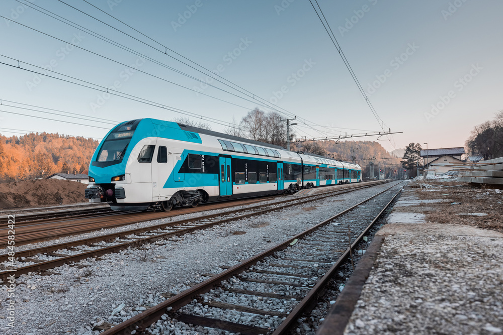 Modern slovenian double decker commuter train is just leaving the rural station of Podnart. Cold and early afternoon in northern Slovenia. Modern slovenian double decker commuter train is just leaving the rural station of Podnart. Cold and early afternoon in northern Slovenia.
