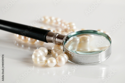 pearls necklace and magnifying glass on white backgrond, pawnshop concept