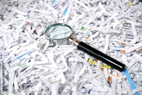 Shredded documents to protect confidential information and magnifying glass, background, top view