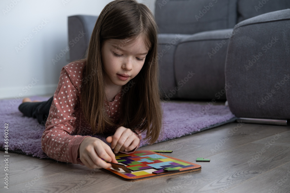 a little girl lies on the floor and collects a wooden tetris puzzle