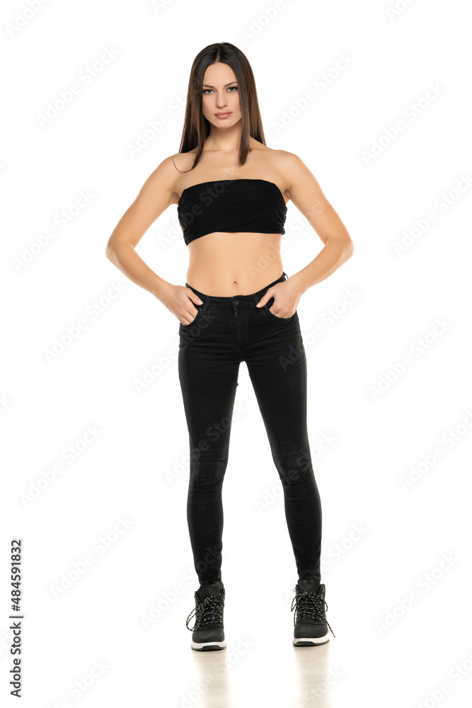 Front view of a young woman in black jeans and short top posing on a white Front view of a young woman in black jeans and short top posing on a white