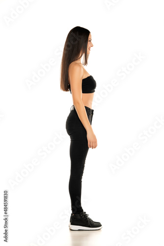 Side view of a young woman in black jeans and short top posing on a white