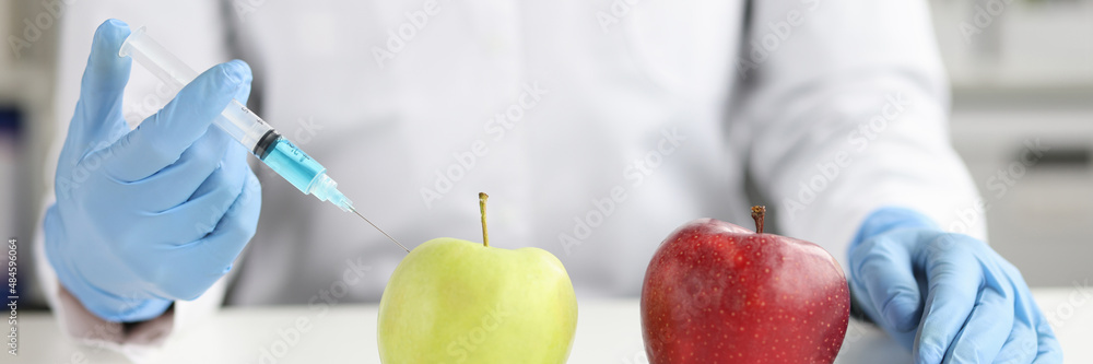 Scientist in white coat makes an injection into green apple in laboratory closeup Scientist in white coat makes an injection into green apple in laboratory closeup