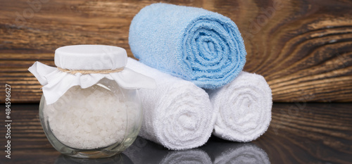 on a dark wooden background, a towel wrapped in a roll and white bath salt in a glass jar, for relaxation