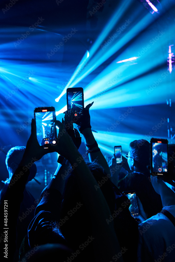the crowd at the concert in neon blue lights with their phones up and filming what is happening. concert, fun, club, dancing the crowd at the concert in neon blue lights with their phones up and filming what is happening. concert, fun, club, dancing