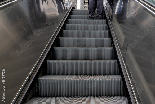 Low angle of a man standing on step of escalator in subway or metro, Vertical transportation in the form of a moving staircase which carries people between floors of a building.