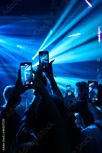 the crowd at the concert in neon blue lights with their phones up and filming what is happening. concert, fun, club, dancing