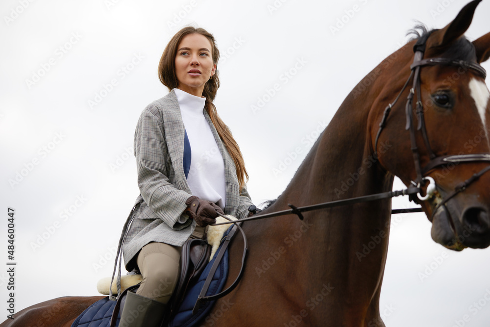 Obraz premium Beautiful young woman riding a horse outdoor. Concept of animal care. Rural rest and leisure. Idea of green tourism. Young european woman wearing helmet and uniform.