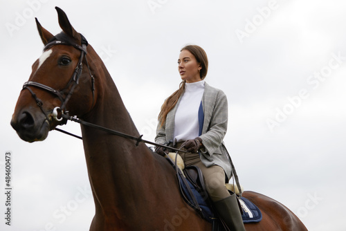 Beautiful young woman riding a horse outdoor. Concept of animal care. Rural rest and leisure. Idea of green tourism. Young european woman wearing helmet and uniform.