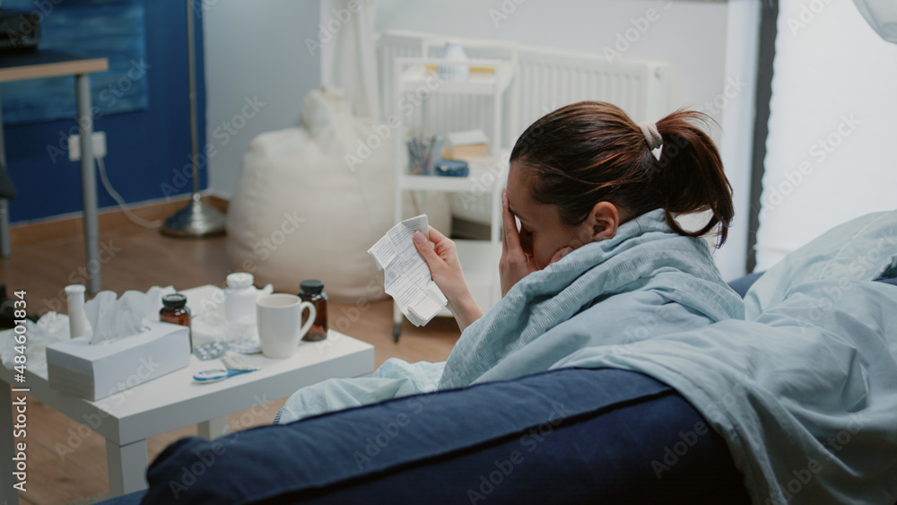 Ill woman reading package leaflet for information about medication and healing treatment. Person with virus symptoms holding medical paper while having pills and capsules on table. Ill woman reading package leaflet for information about medication and healing treatment. Person with virus symptoms holding medical paper while having pills and capsules on table.