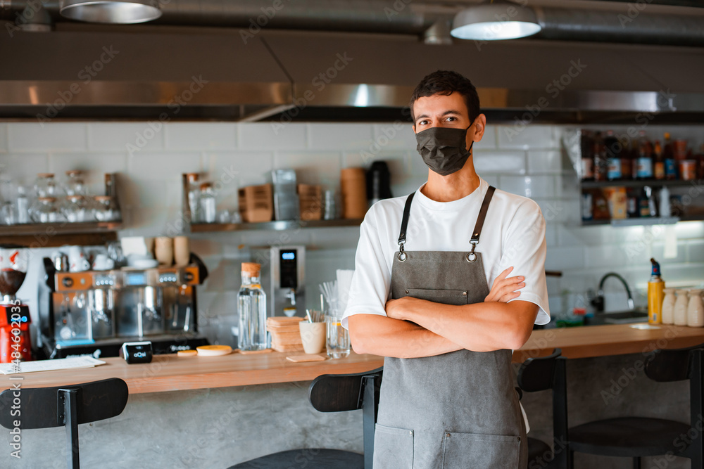 Young man coffee shop owner or barista in face mask and apron working during covid-19 pandemic