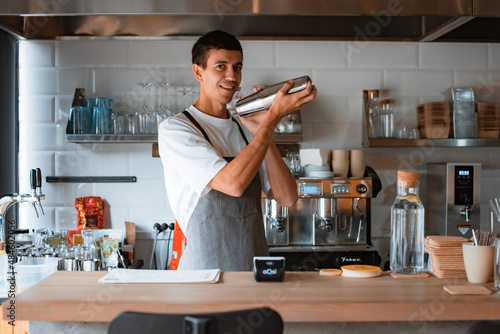 Smiling professional male barista making caramel iced frappe while working in local coffee shop