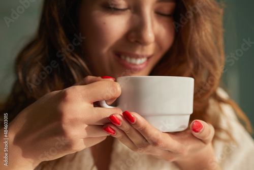 Cheerful woman smelling coffee at home