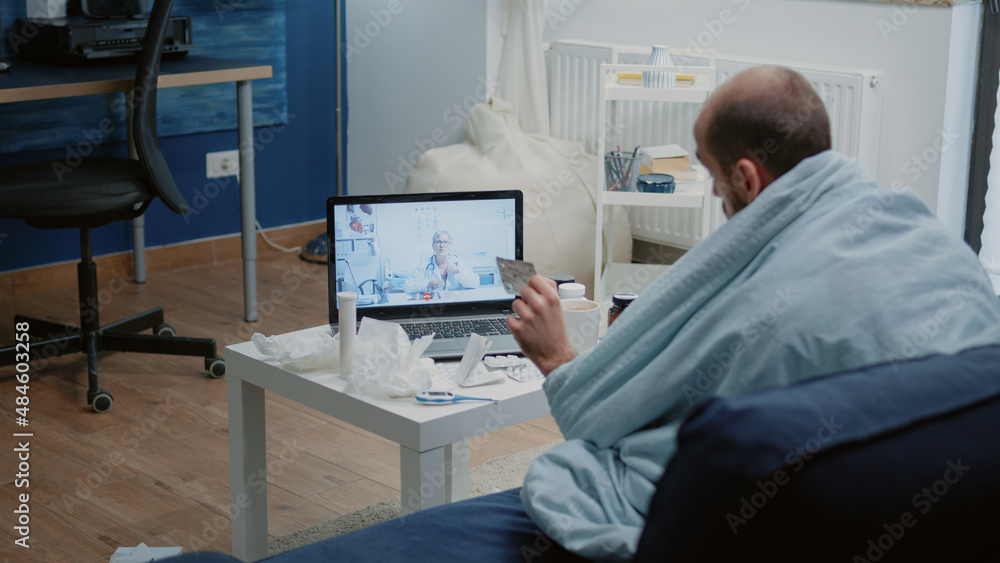 Ill patient talking on video call conference for telehealth using laptop. Man holding capsule tablet, asking doctor about prescription medicine and treatment while using online remote conference