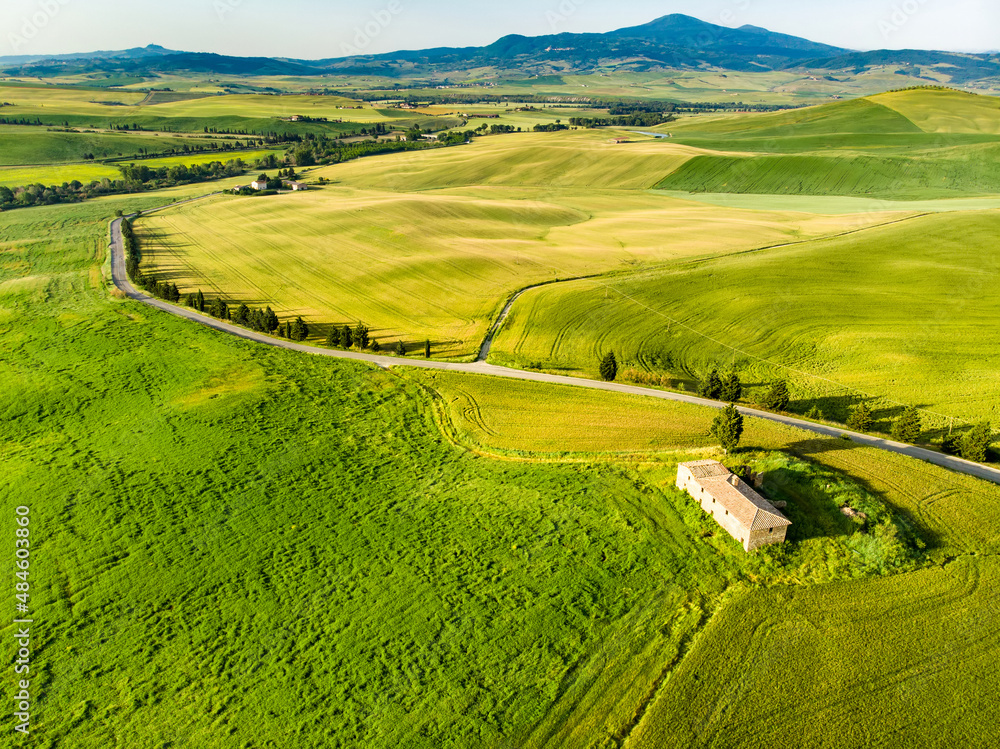 Stunning aerial view of green fields and farmlands with small villages on the horizon. Rural landscape of rolling hills, curved roads and cypresses of Tuscany, Italy.