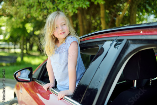 Funny young girl sticking her head out the car window looking forward for a roadtrip or travel. © MNStudio