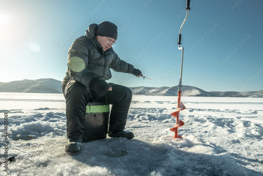 Fisherman is fishing in a hole on the ice of a large frozen lake on a sunny  day. The joy of winter fishing Stock Photo