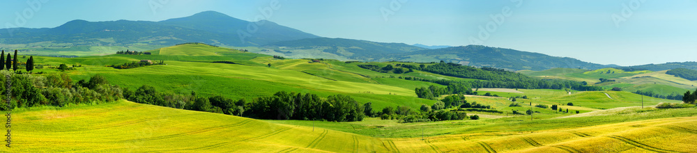 Stunning view of fields and farmlands with small villages on the horizon. Summer rural landscape of rolling hills, curved roads and cypresses of Tuscany, Italy.