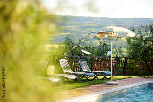 Round beige sunshade and several folding beach chairs by the outdoor pool in agriturismo overlooking fields and farmlands of Tuscany, Italy. photo