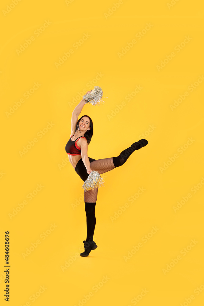 Beautiful cheerleader in costume holding pom poms on yellow background