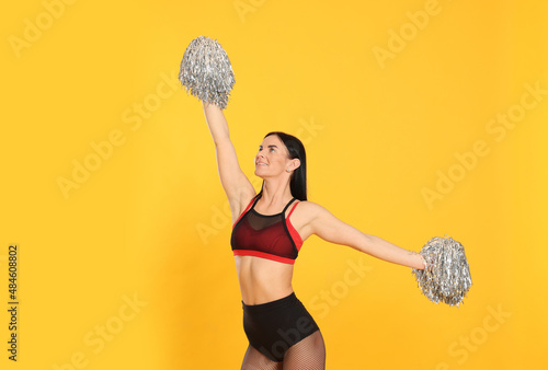 Beautiful cheerleader in costume holding pom poms on yellow background photo
