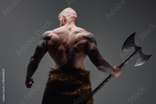 Tattooed viking with steel axe his back facing to camera photo