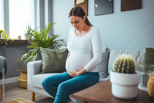 The woman feels stomach pain while working in the office, her hands touch her stomach and the awareness of her pregnancy. She is considering a visit to the doctor photo