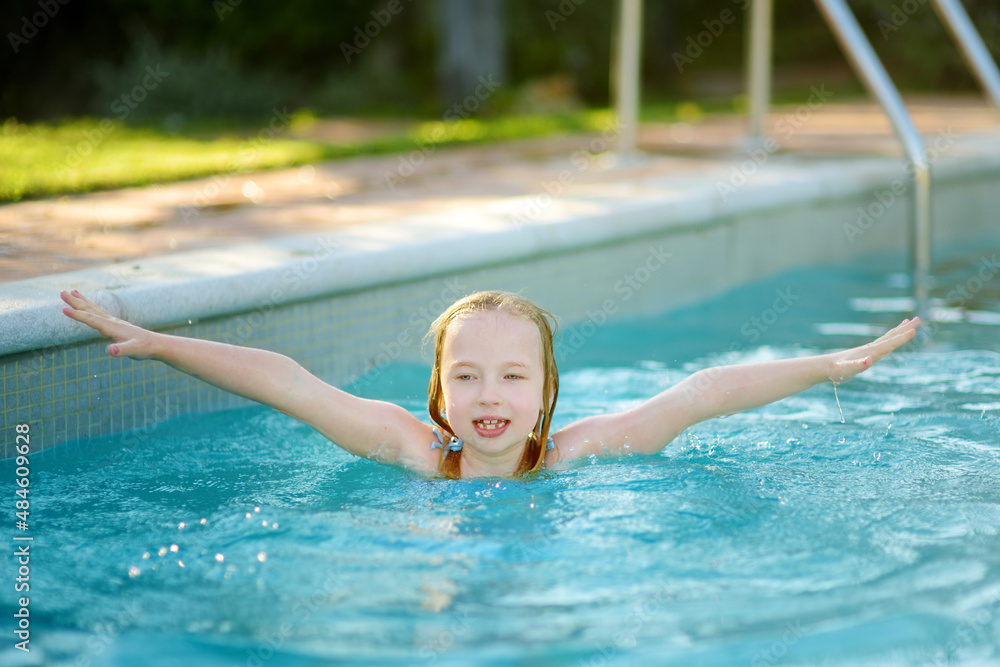 Cute young girl having fun in outdoor pool. Child learning to swim. Kid having fun with water toys. Family fun in a pool. Summer activities for family with kids.