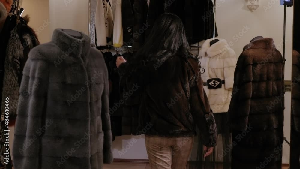 Young woman trying on fur coat in women's clothes store. Young european woman choosing best fur coat in women's clothing store. Young woman trying on fur coat in women's clothes store. Young european woman choosing best fur coat in women's clothing store.