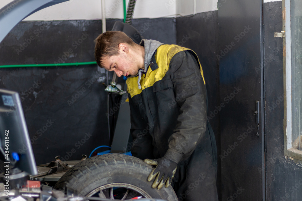 Young mechanician changing car wheel in auto repair shop using equipment