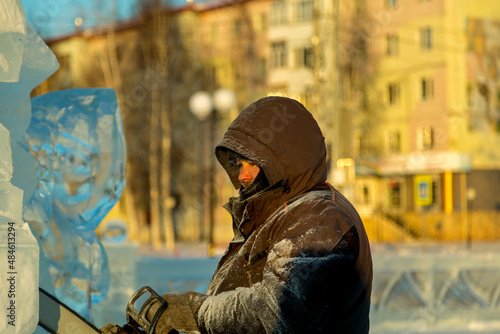 The sculptor cuts a figure from an ice block with a gasoline saw