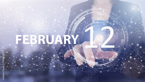 February 12nd. Day 12 of month, Calendar date. Hand click luminous hologram calendar date on light blue town background. Winter month, day of the year concept. photo