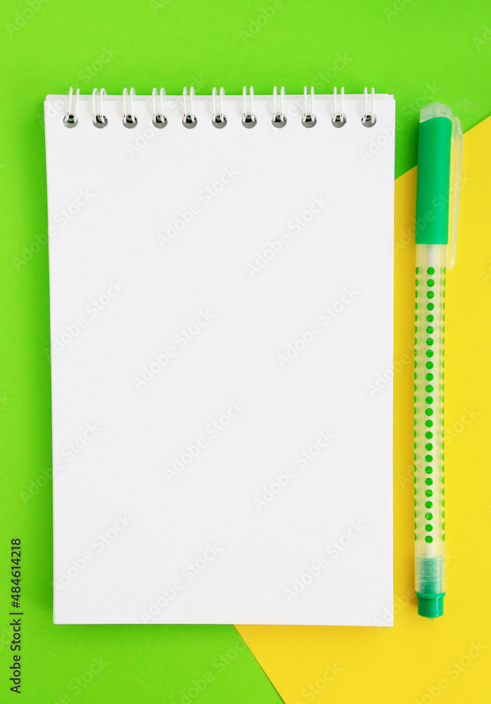 Fototapeta Nowy pusty arkusz notatnika z miejscem na tekst obok zielonego długopisu. Tło w dwóch kolorach zielonym i żółtym. Powrót do szkoły