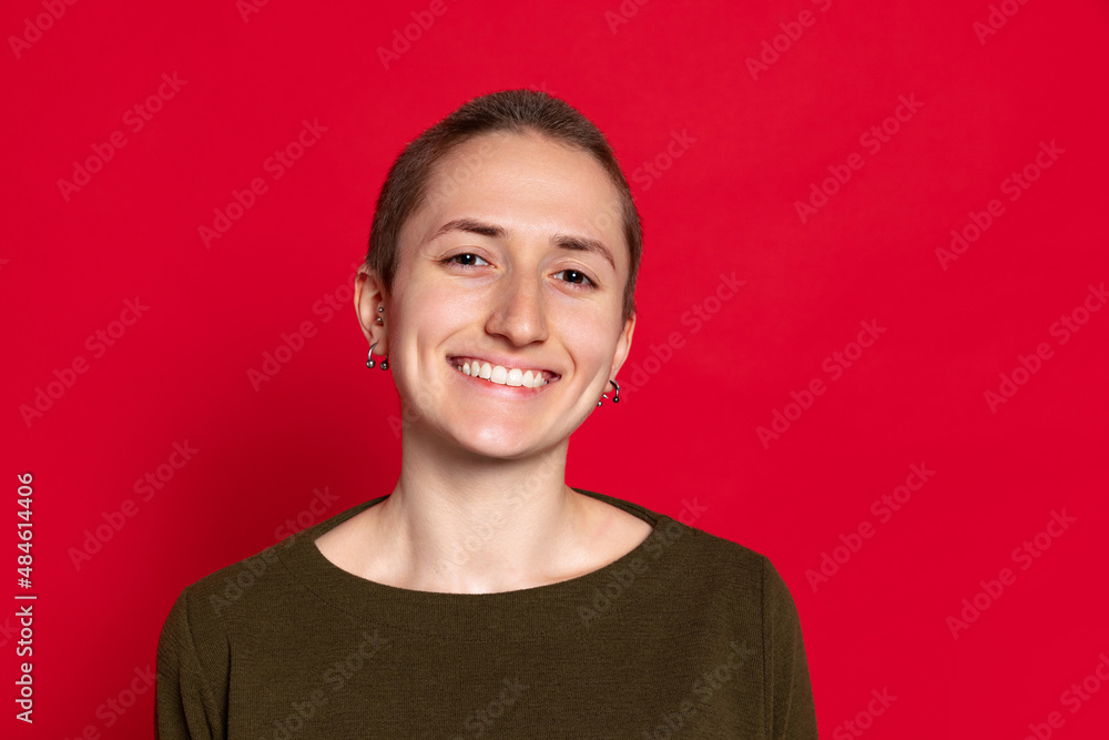 Portrait of young smiling woman, student with short hair in dark sweater isolated on red background. Concept of emotions, studying, ad Portrait of young smiling woman, student with short hair in dark sweater isolated on red background. Concept of emotions, studying, ad