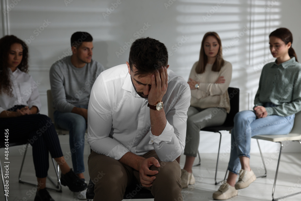 Unhappy man and group of people behind his back indoors. Therapy session Unhappy man and group of people behind his back indoors. Therapy session
