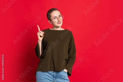 Portrait of young smiling woman, student with short hair in dark sweater isolated on red background. Concept of emotions, studying, ad photo