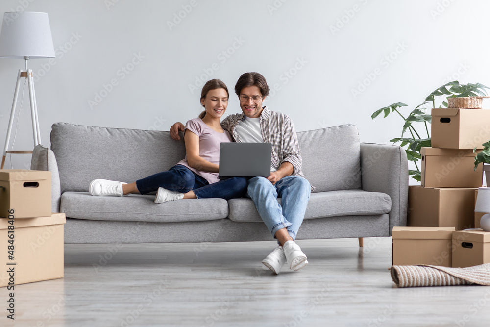 Busy happy european young man show computer to woman on sofa in living room interior