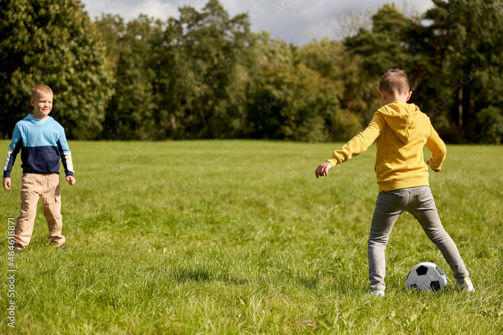 childhood, leisure games and people concept - happy little boys with ball playing soccer at summer park childhood, leisure games and people concept - happy little boys with ball playing soccer at summer park