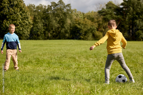 childhood, leisure games and people concept - happy little boys with ball playing soccer at summer park