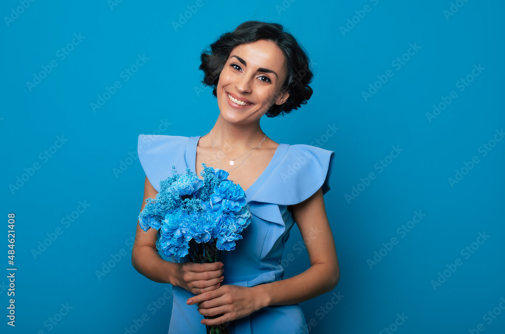 The portrait of a happy excited gorgeous young woman in an elegant blue dress is posing with a fresh bunch of blue flowers. Mothers day. Women's holidays. Springtime. Women rights The portrait of a happy excited gorgeous young woman in an elegant blue dress is posing with a fresh bunch of blue flowers. Mothers day. Women's holidays. Springtime. Women rights