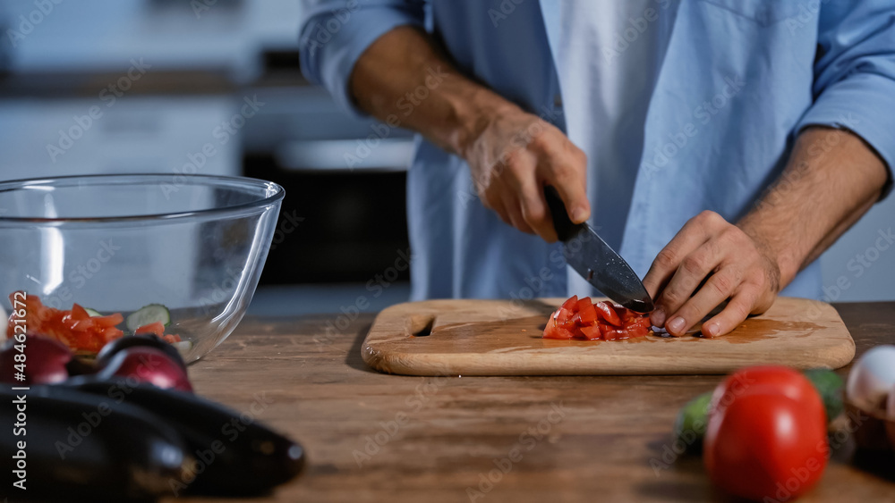 cropped view of man cutting ripe tomatoes near blurred eggplants and glass bowl. cropped view of man cutting ripe tomatoes near blurred eggplants and glass bowl.